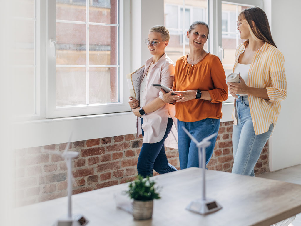 Drei Frauen gehen an einem Tisch mit vorbei auf dem Windradmodelle stehen