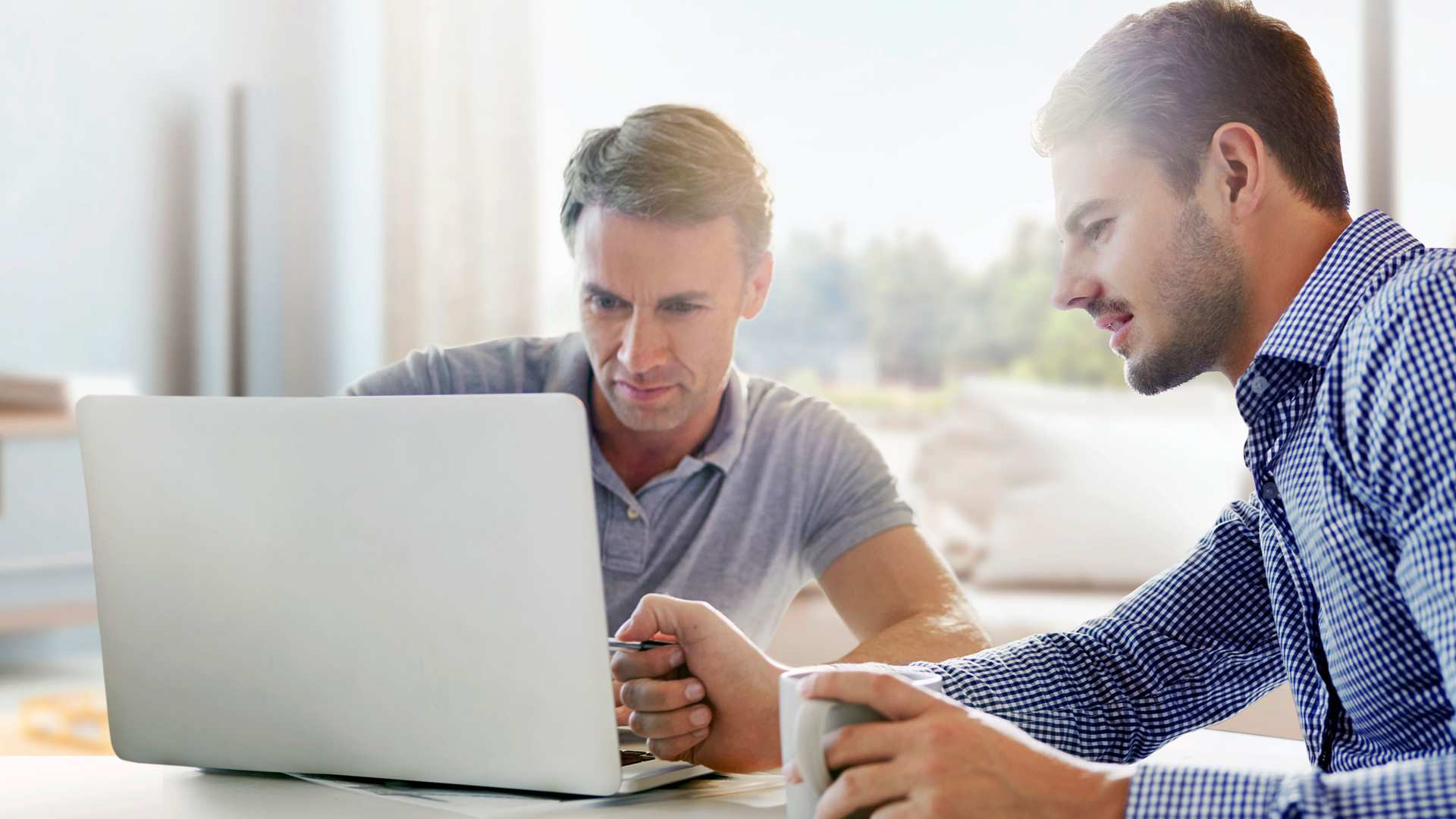 Zwei Männer am Schreibtisch, blicken in ein Notebook